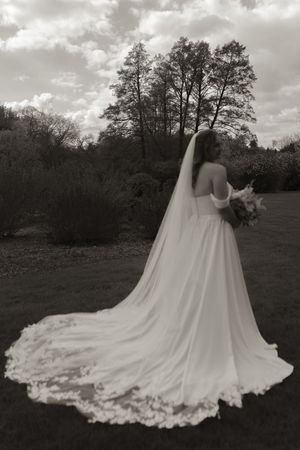 A dramatic back view of a bride in a flowing white gown with a long train against a cloudy sky.