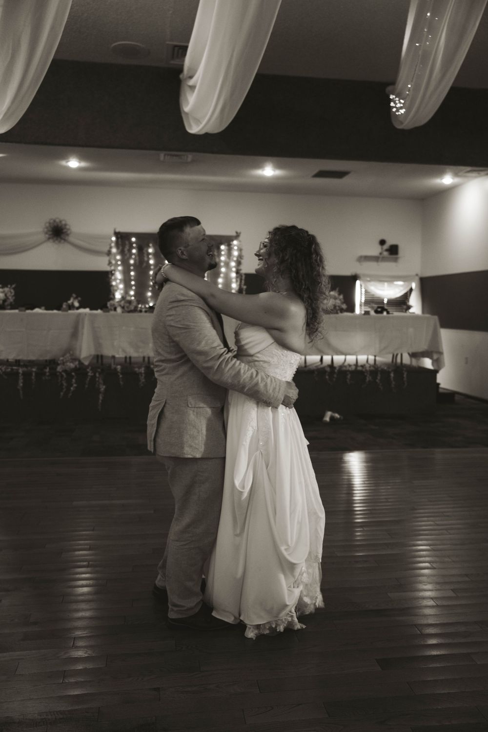 A black and white photo captures a couple's intimate dance moment in a reception venue.