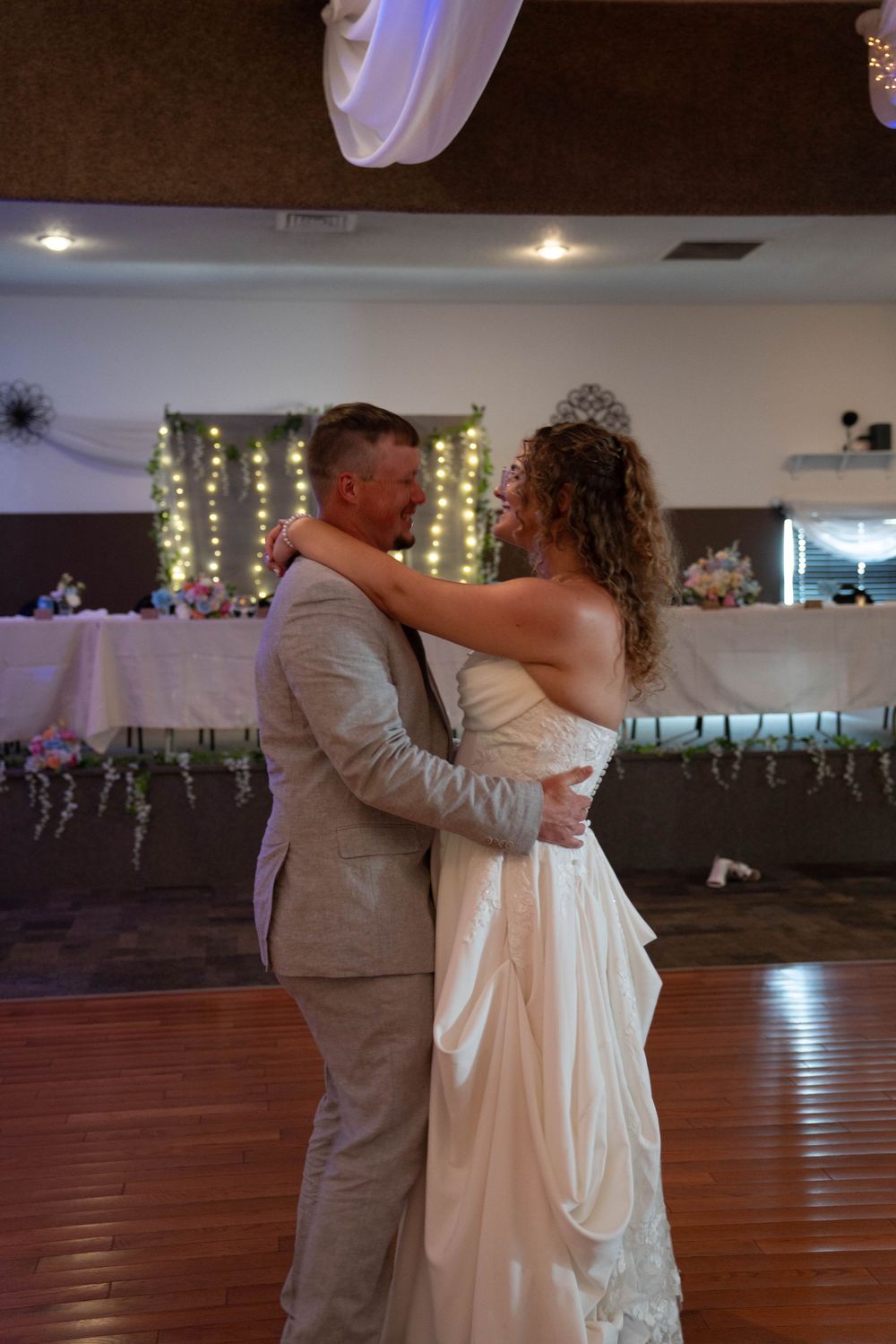 A couple shares their first dance in a beautifully lit reception hall with string lights.