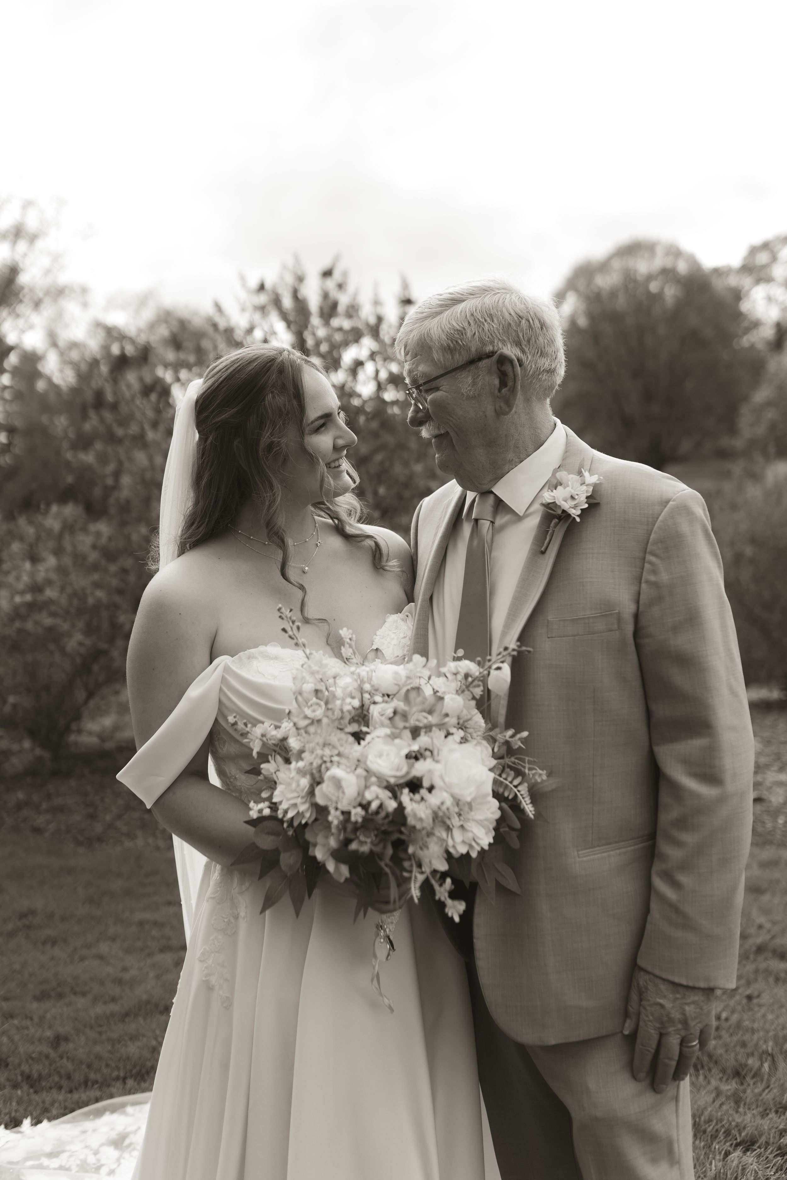 Intimate wedding portrait with couple holding floral bouquet against pastoral landscape.