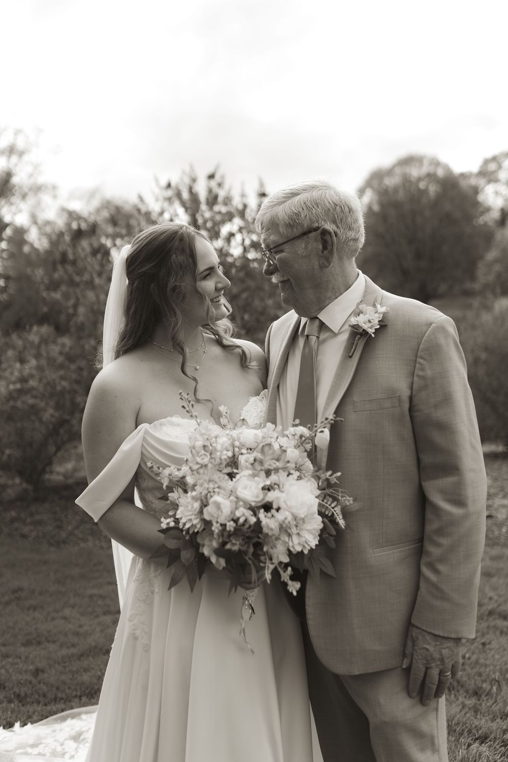 Intimate wedding portrait with couple holding floral bouquet against pastoral landscape.