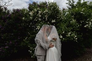 Intimate wedding moment captured in garden setting with white flowers in background.