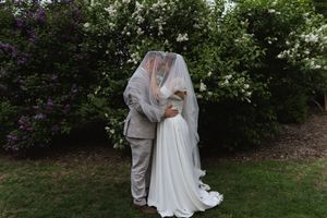 Newlyweds share intimate moment in lush garden setting with white flowers.