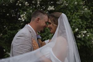 Couple shares romantic moment under flowing veil in garden setting.