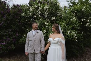 Wedding couple poses in front of blooming garden with white flowers and greenery.