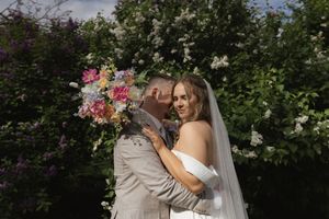 Wedding couple embraces in front of blooming garden with white and pink flowers.