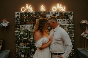 Romantic indoor wedding reception scene with illuminated signage and photo wall.