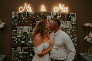 Wedding reception venue decorated with glowing script signage and photo wall display.