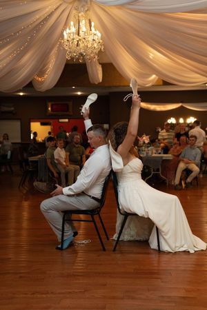 Wedding guests playing a fun party game with chairs at a reception with draped ceiling decor.