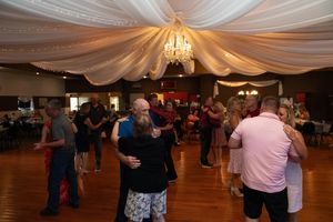 Wedding guests dancing in pairs on a wooden dance floor under draped fabric ceiling decor.