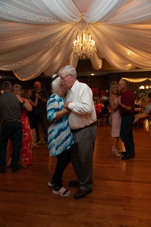 Couples slow dancing at a wedding reception under elegant white draped ceiling and chandeliers.