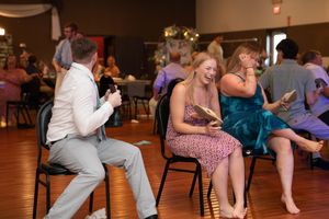 Wedding party members playing a reception game with chairs on hardwood floors.