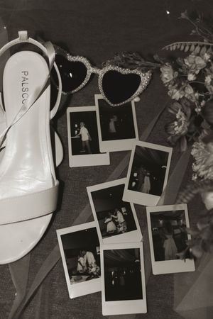 Black and white photo of scattered polaroid photos and wedding decor elements.