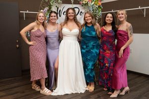 Wedding party wearing colorful dresses in shades of purple, teal, and pink pose together at a celebration.