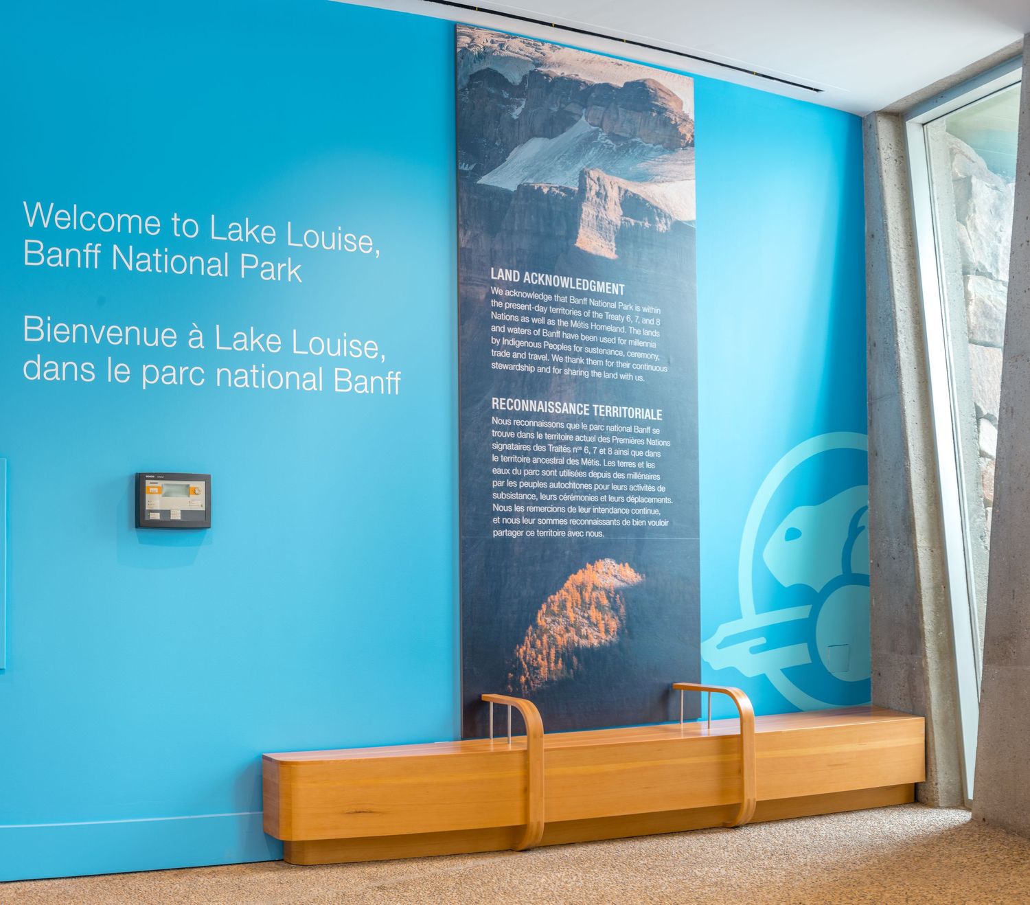 Museum exhibit displays mountain landscape with autumn trees and lighting fixture in modern gallery space.