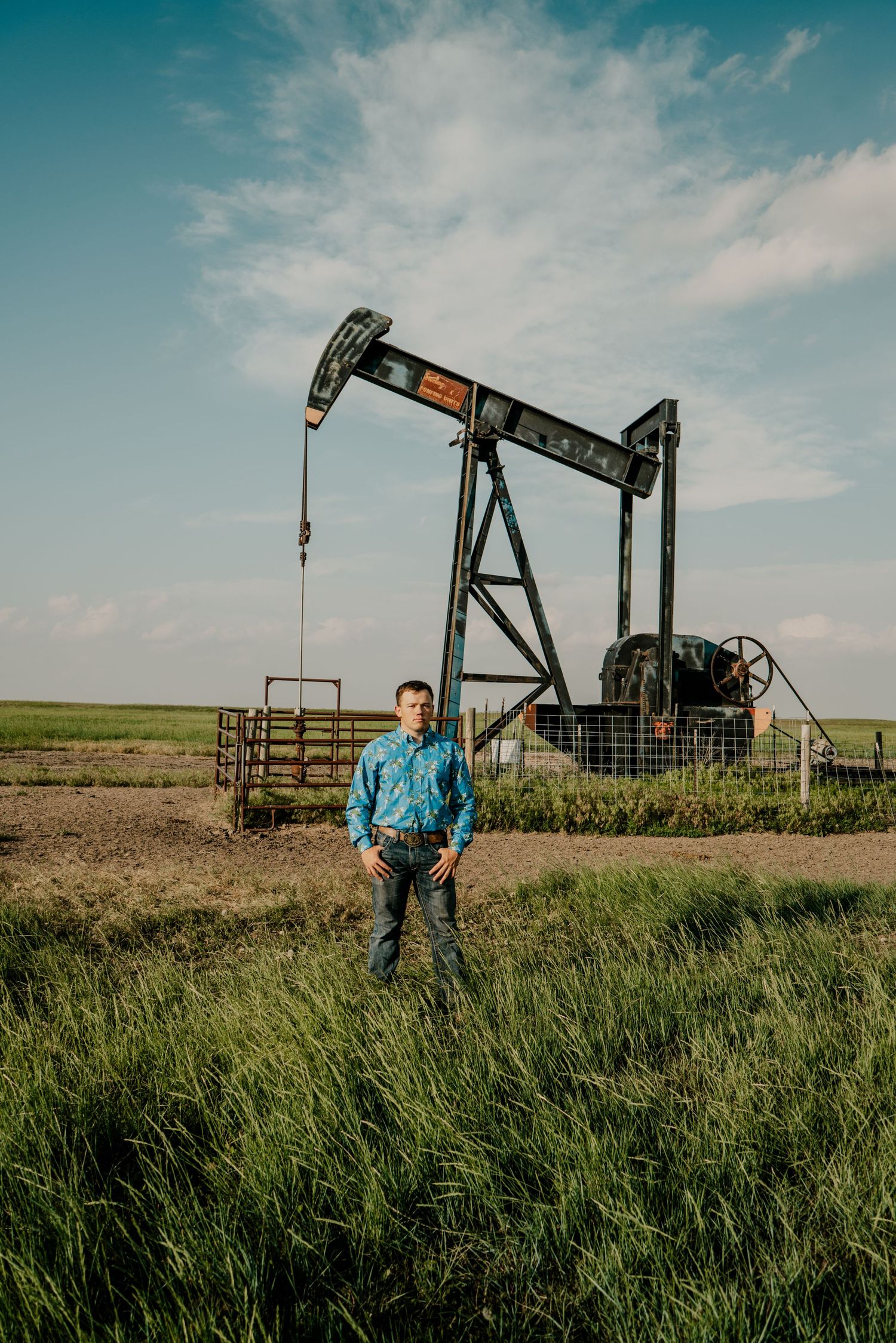 A young man standing in front of a oil well with bright blue sky in the background