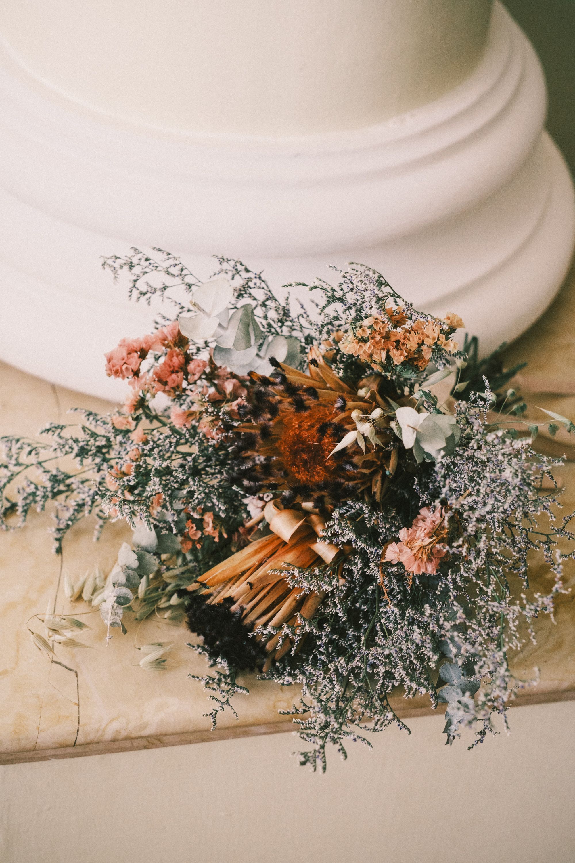 Rustic wedding bouquet with dried flowers and soft orange tones against white backdrop.