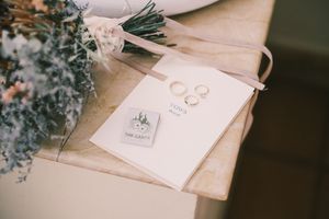 Wedding details flat lay with rings, invitation and flower stems.