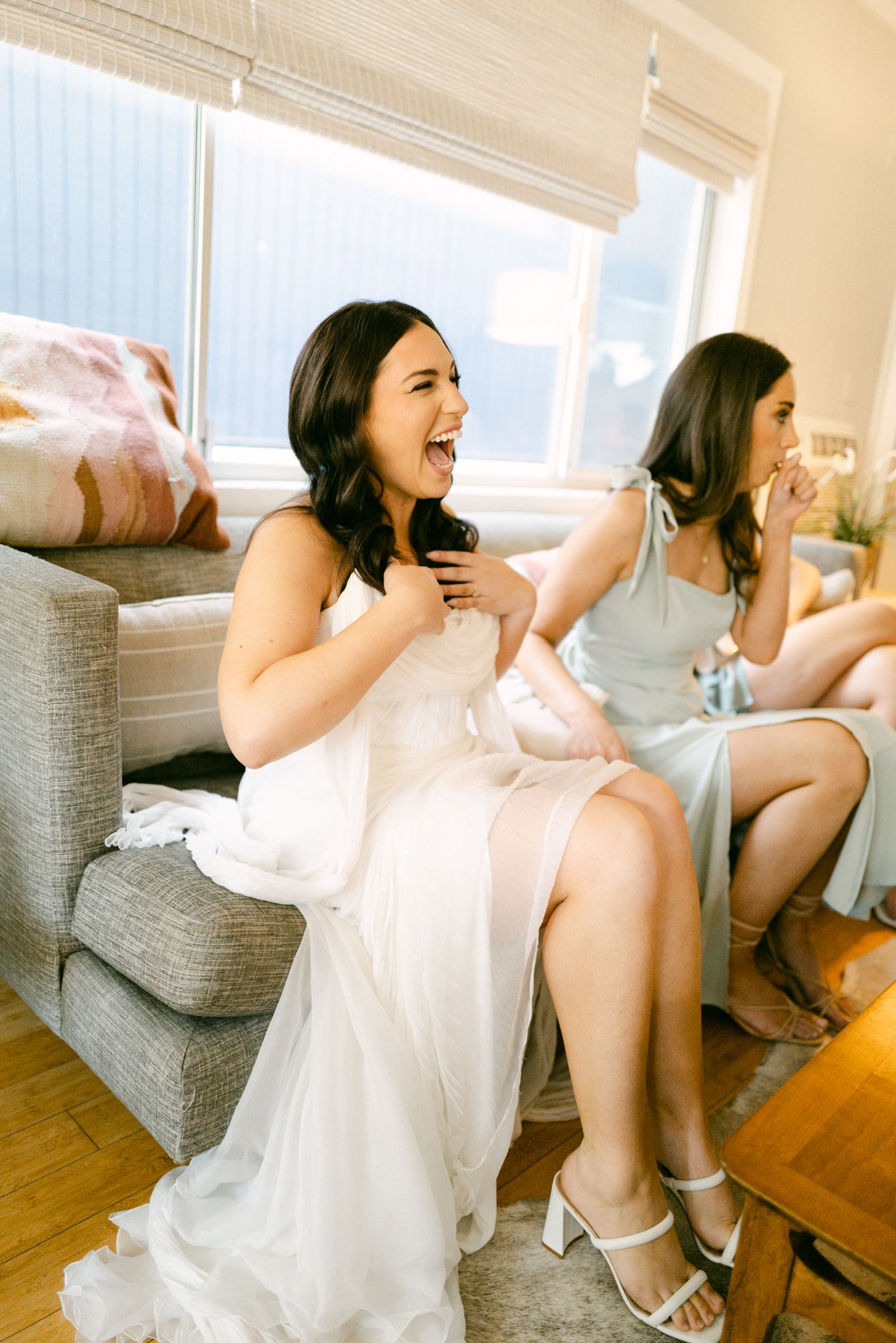 Wedding party members laugh and celebrate while getting ready in a bright room.
