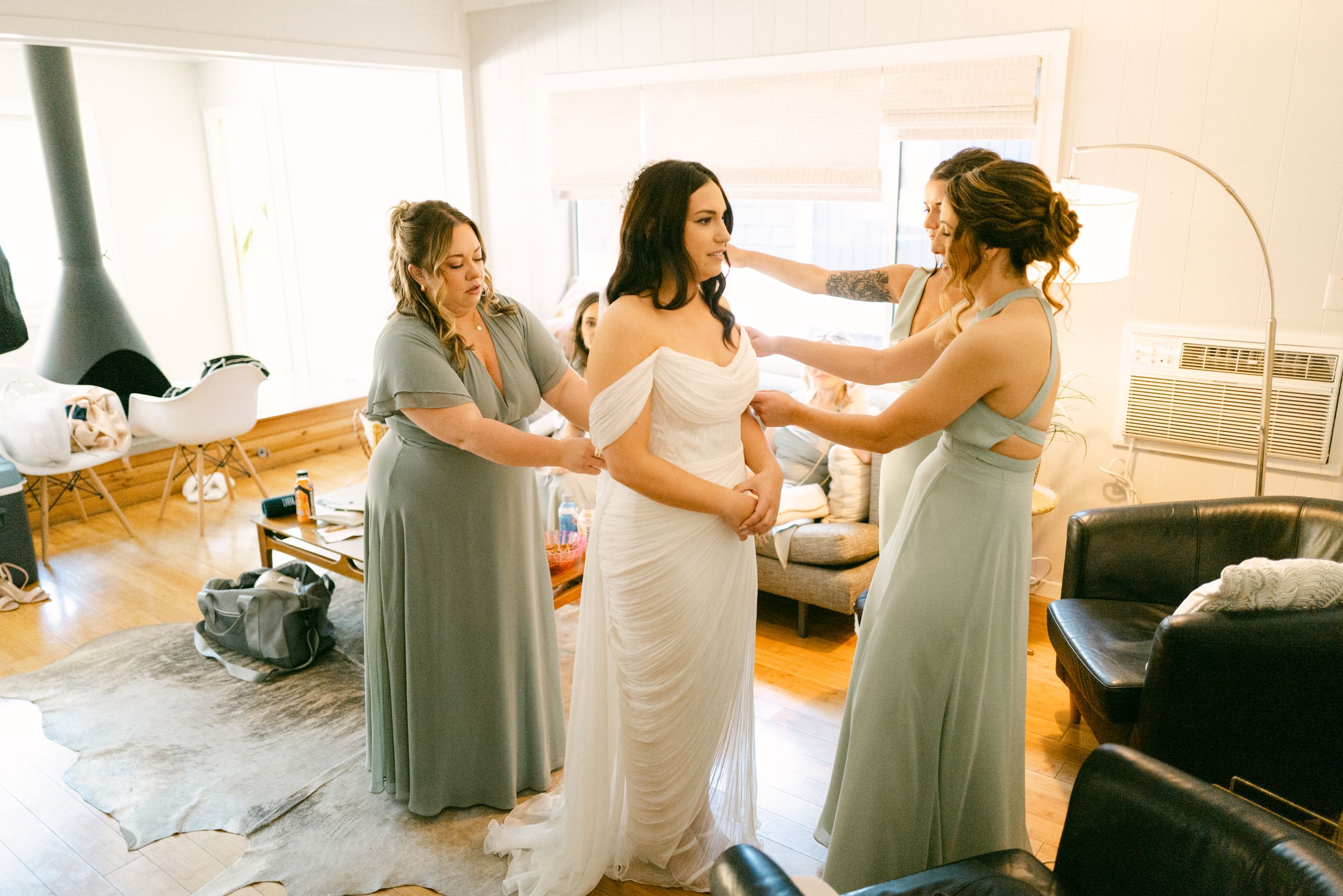 Bridesmaids in sage green dresses help the bride prepare for the wedding.