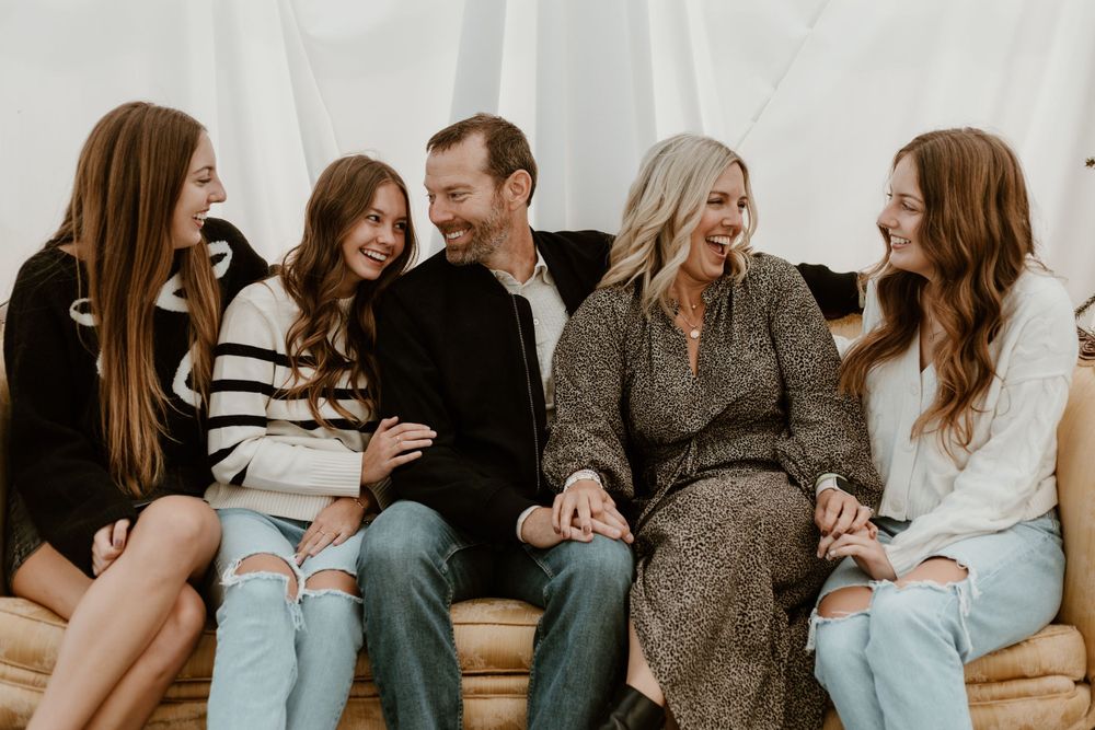 Happy family of five laughing together while sitting on couch in casual portrait session.