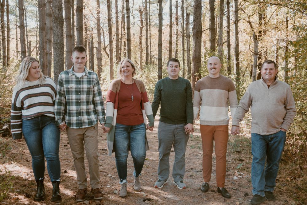 Six family members walk together smiling on a wooded autumn path in coordinated fall outfits.