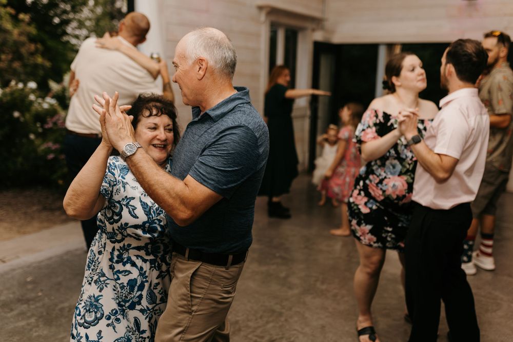 An older couple dances together joyfully at an outdoor wedding reception celebration.