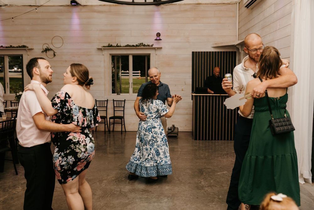 Couples dance together in a white barn wedding reception venue with string lights.