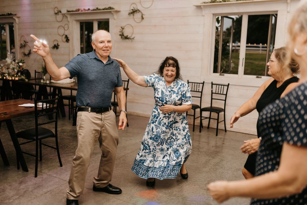 An older couple dances energetically with guests at a elegant wedding reception celebration.
