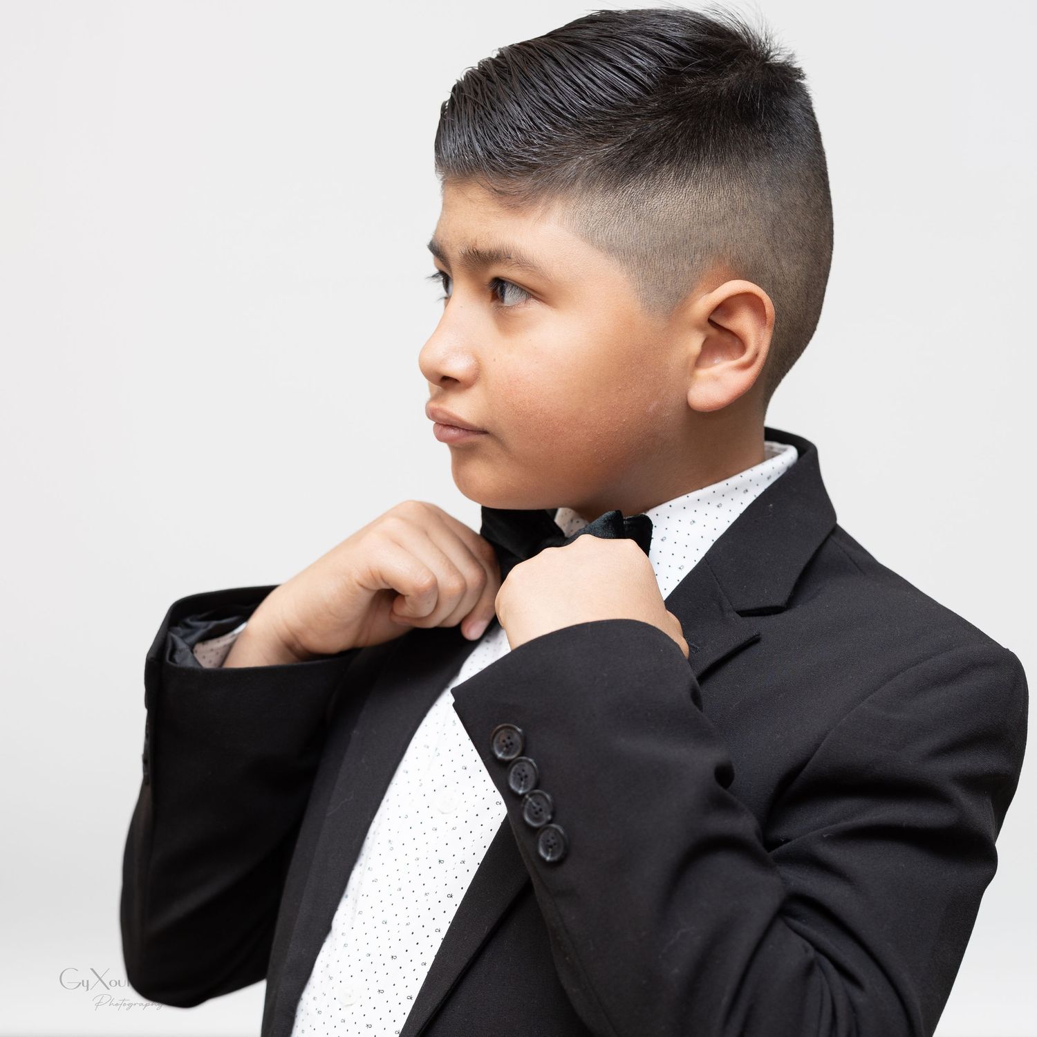 Young person in formal black suit and white tie adjusts their bowtie in a side profile pose.
