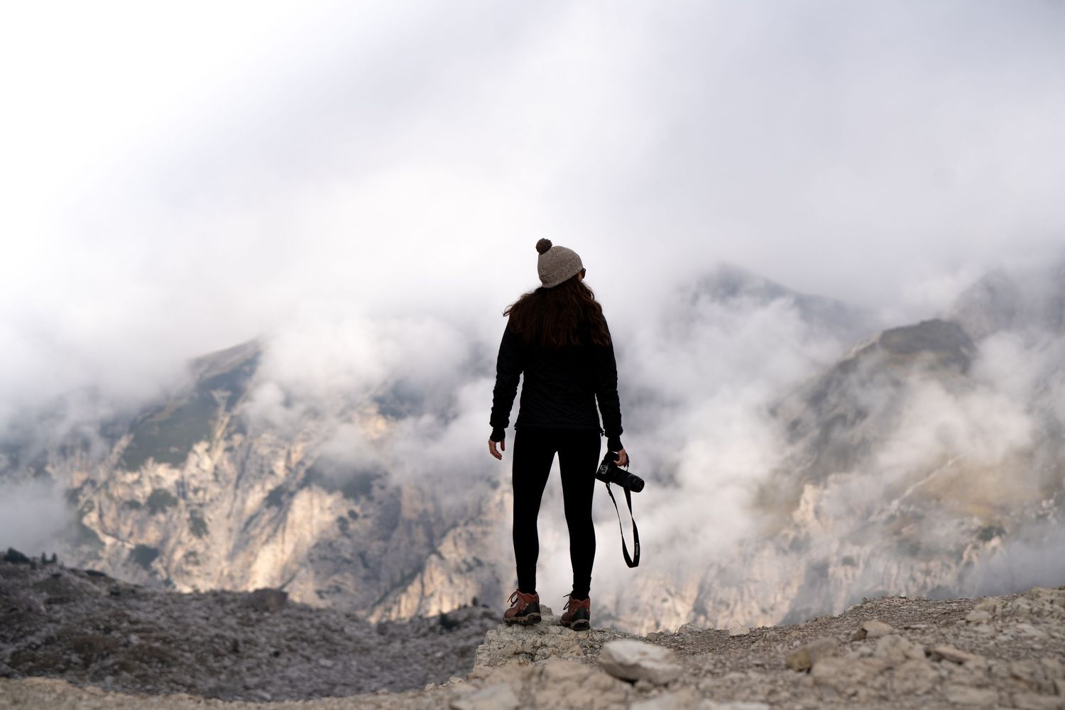 Adventure photography: a silhouetted woman gazes over a smoky mountain landscape holding her camera in her hand.