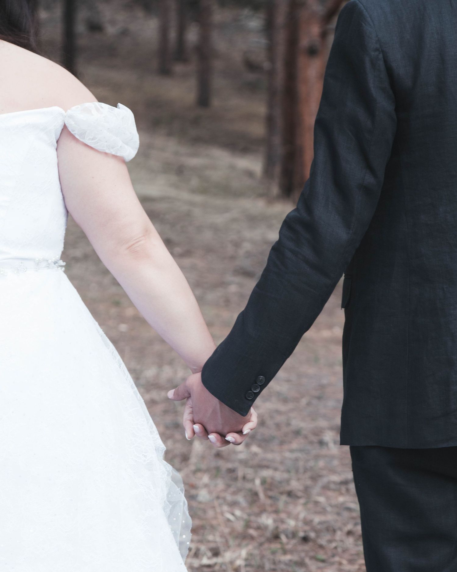 A couple holds hands during their wedding ceremony, with the bride in white and groom in black suit.