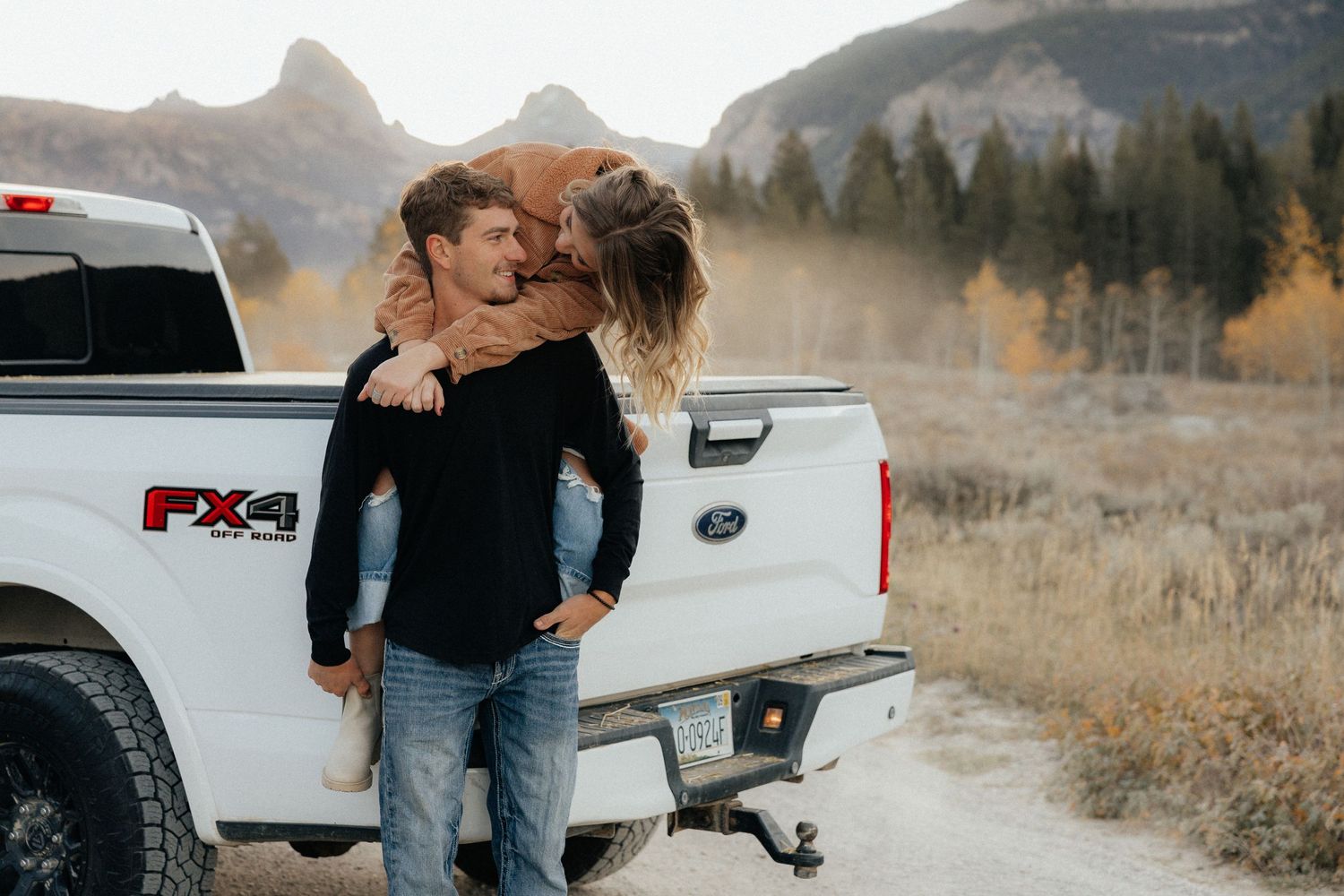 A couple shares an intimate moment by their pickup truck in a mountain setting.