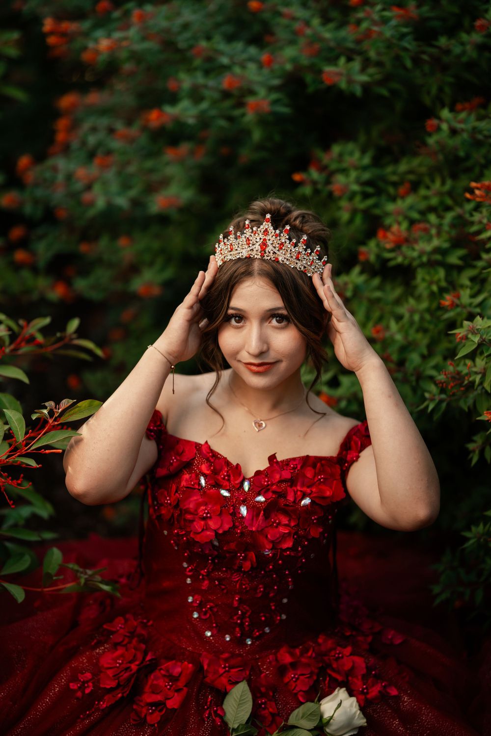 A red formal gown adorned with sparkles and embellishments in a garden setting with red flowers in background.