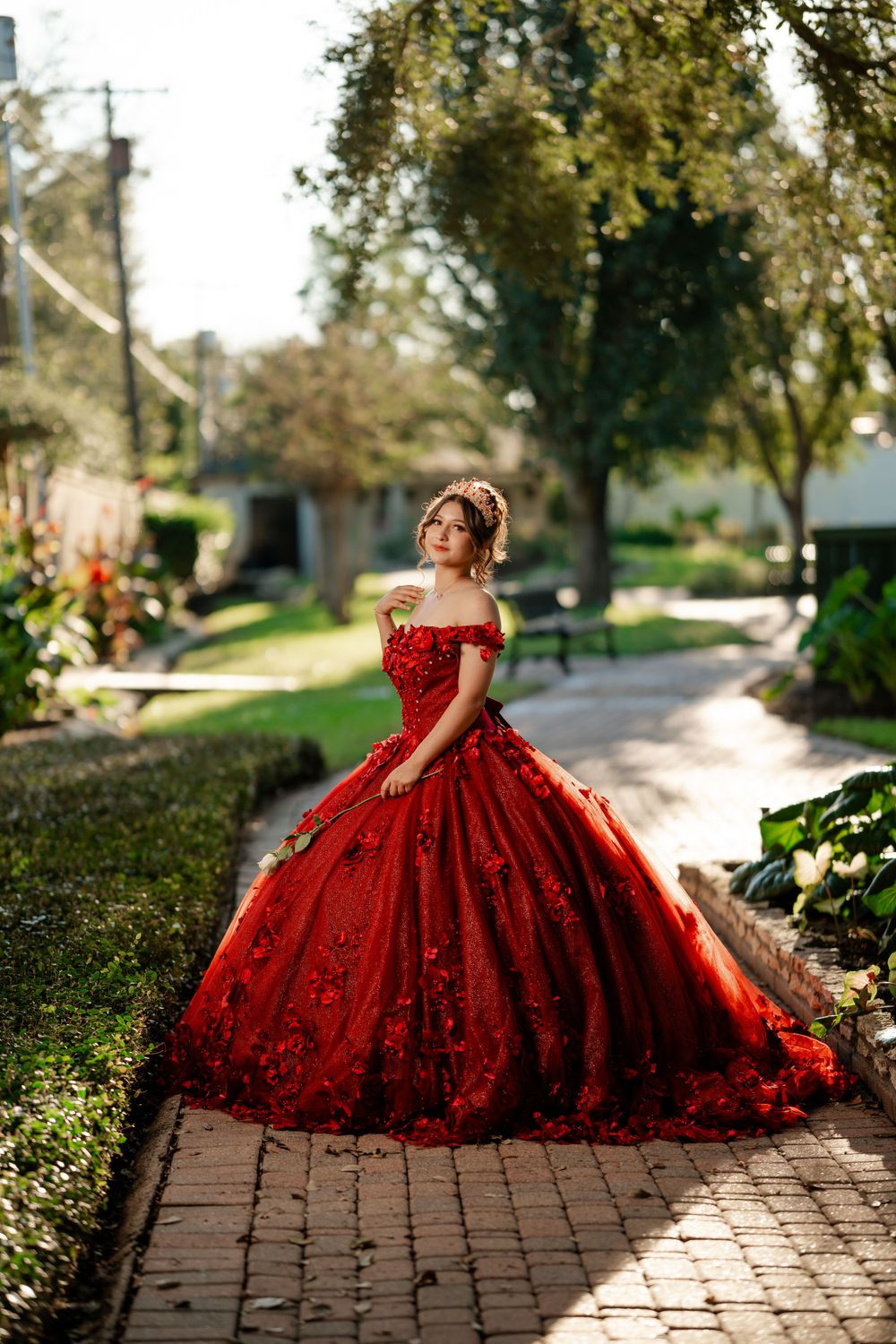 An elegant red quinceañera dress with a voluminous skirt captured on a garden pathway during golden hour.