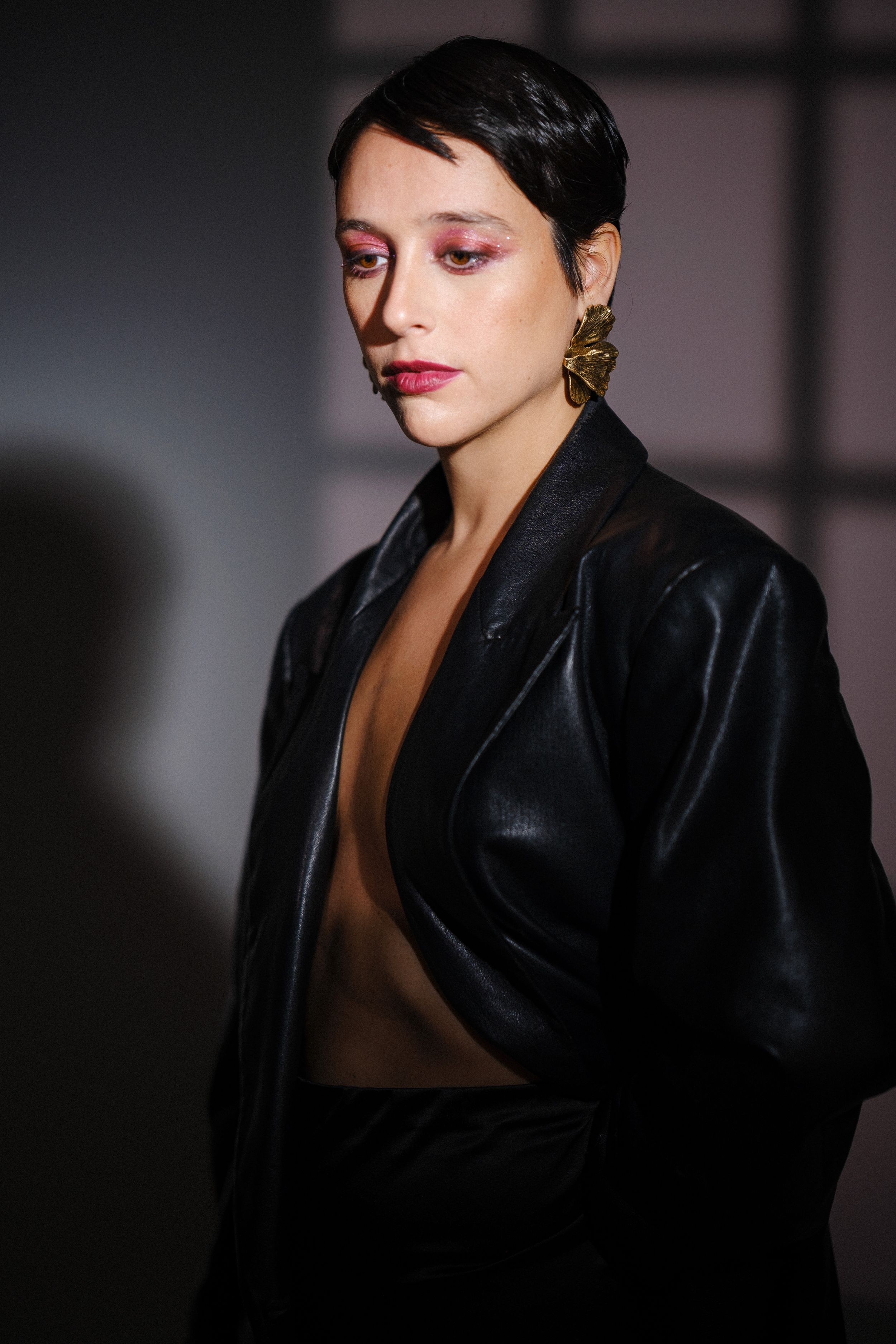Dramatic portrait in black jacket with bold red lips and gold earring.