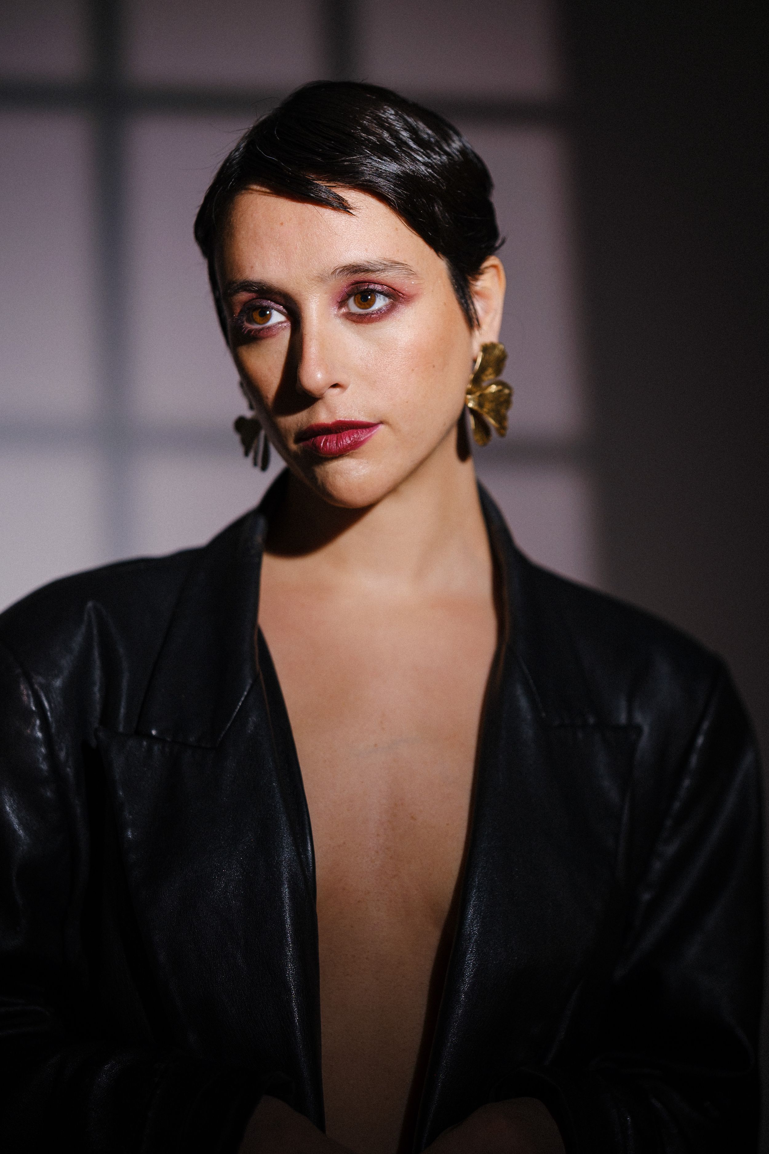 Fashion portrait with bold makeup and black jacket against shadowy background.