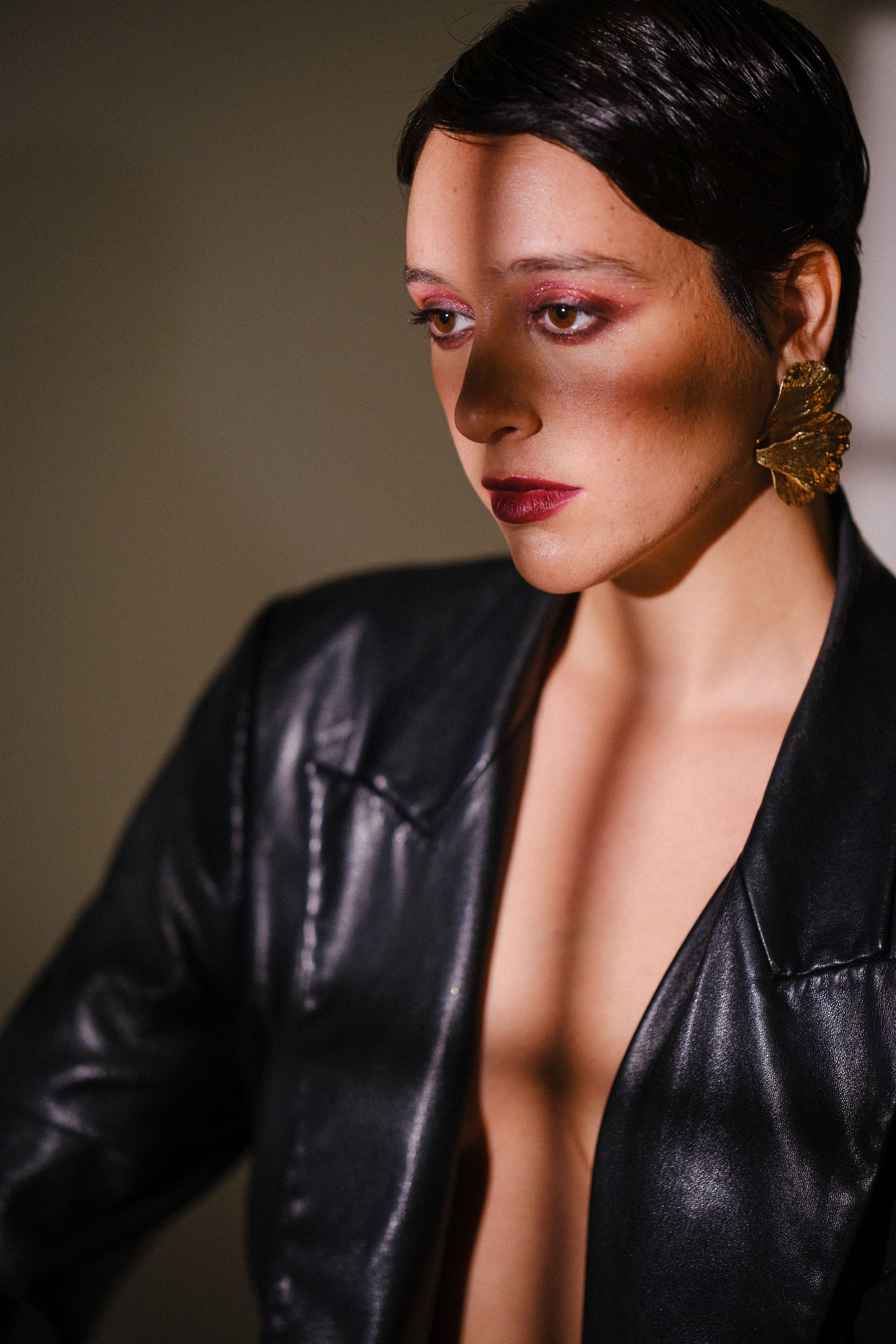 Fashion model wearing black leather jacket poses dramatically against neutral background.