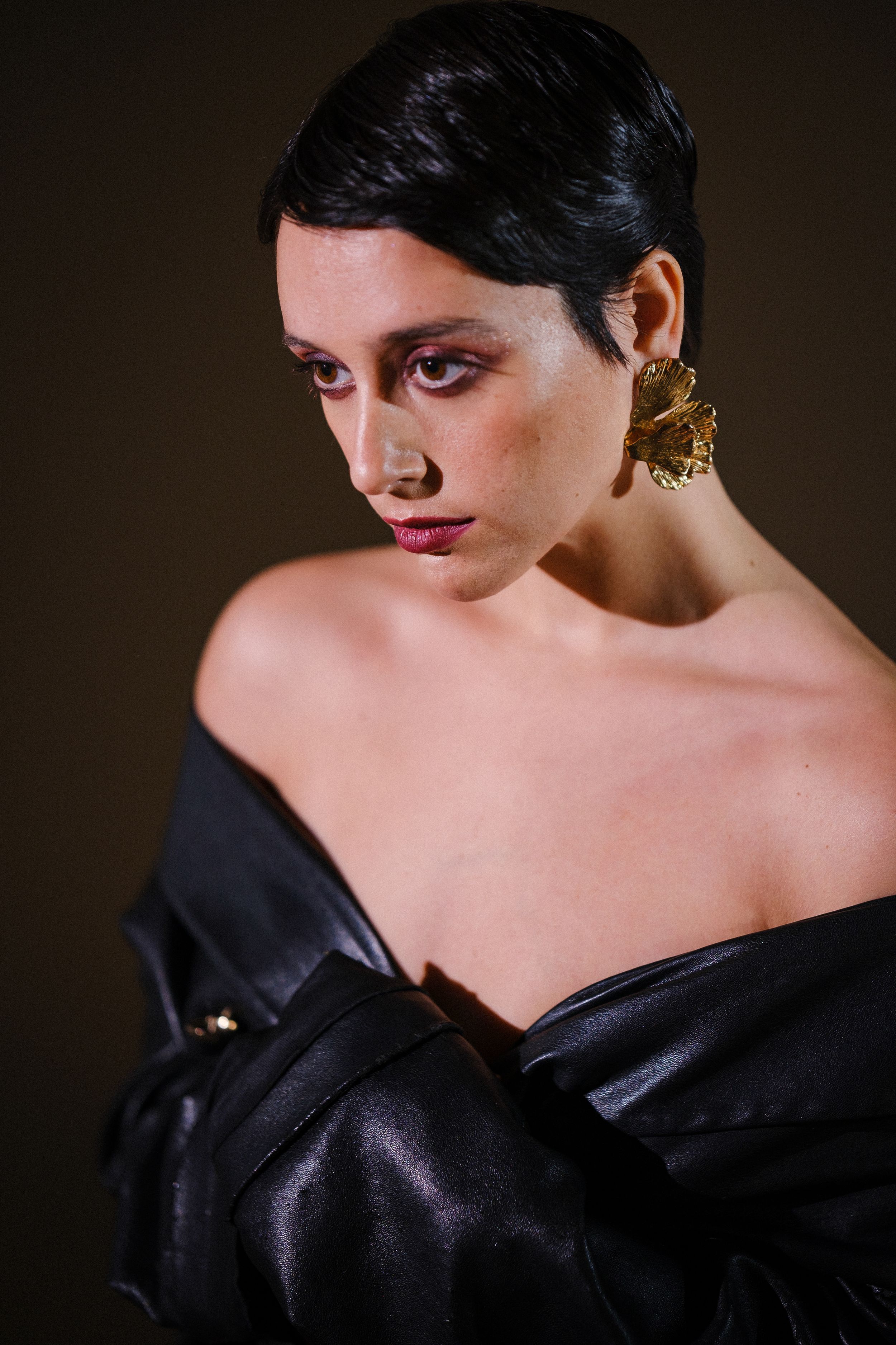 Close-up shot of model in black off-shoulder jacket with gold earring.