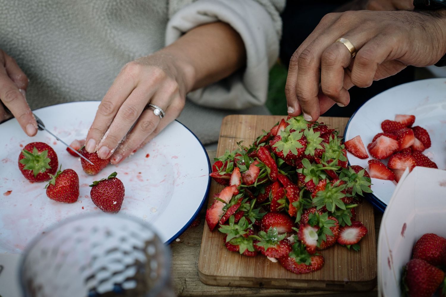 Fresh strawberries being prepared on a wooden cutting board with herbs.