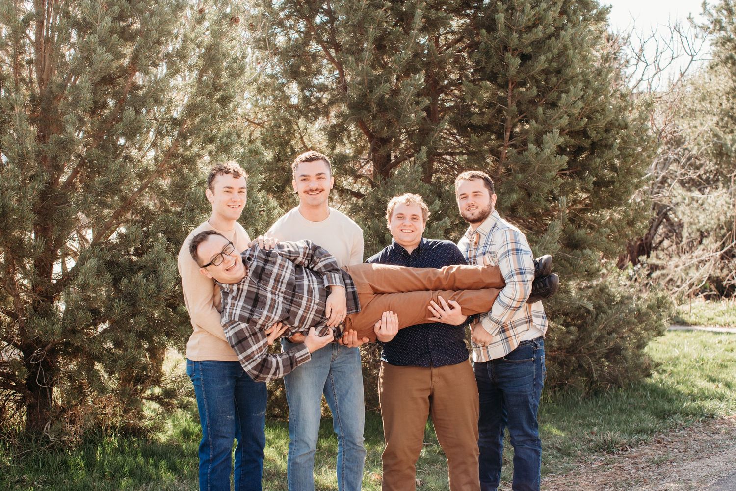 Group of people carrying wooden furniture outdoors among evergreen trees.