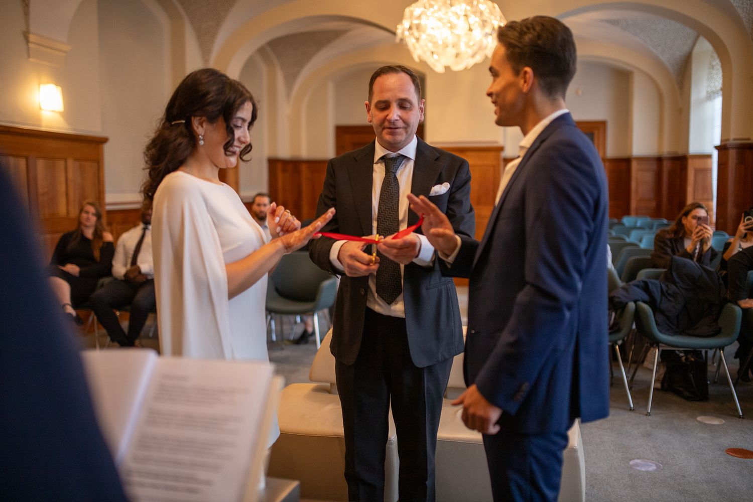 Wedding guests dance and mingle in an elegant ballroom with arched ceilings and warm lighting.
