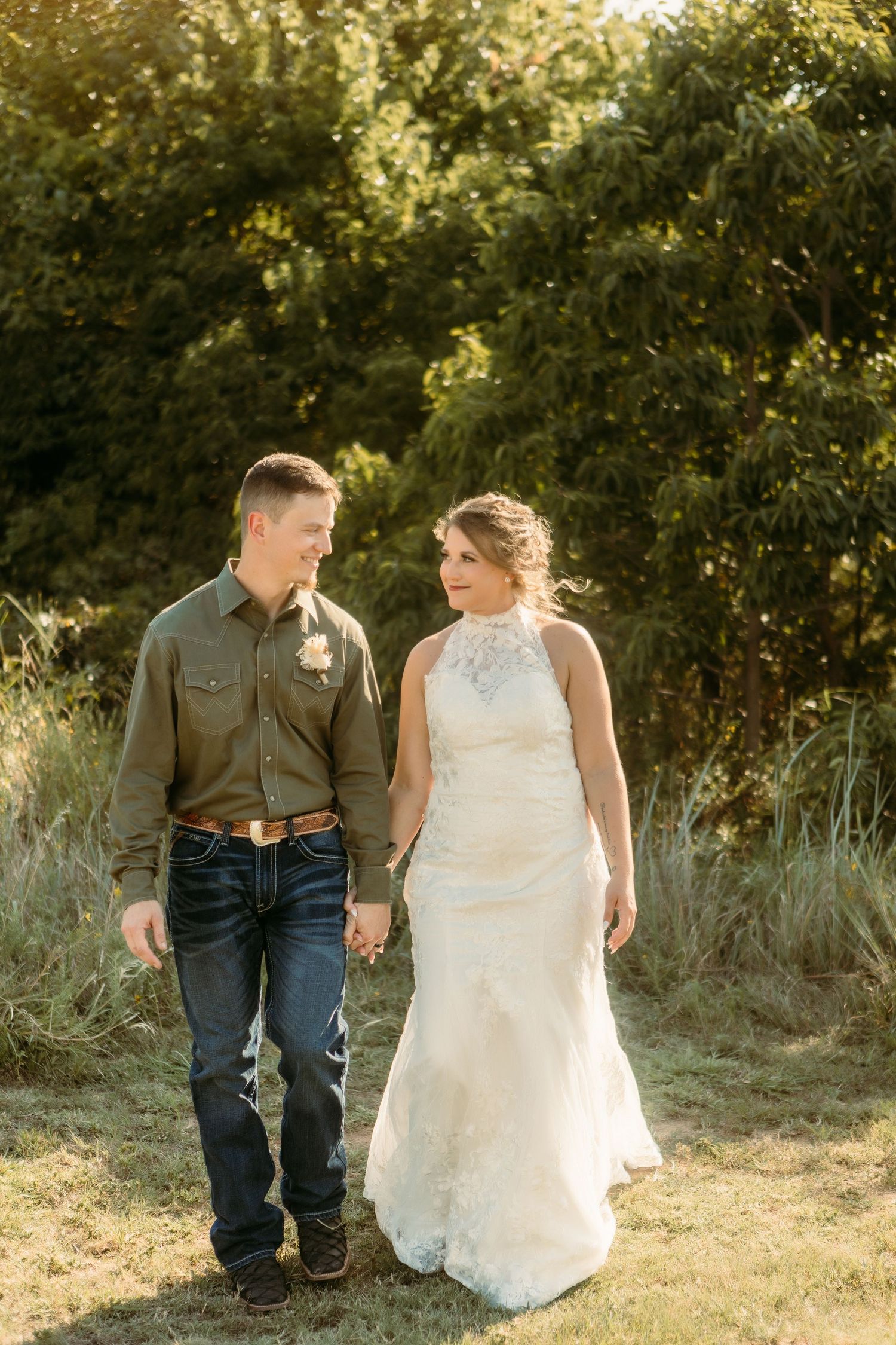 A couple in wedding attire sitting together on grass during golden hour at an outdoor venue.