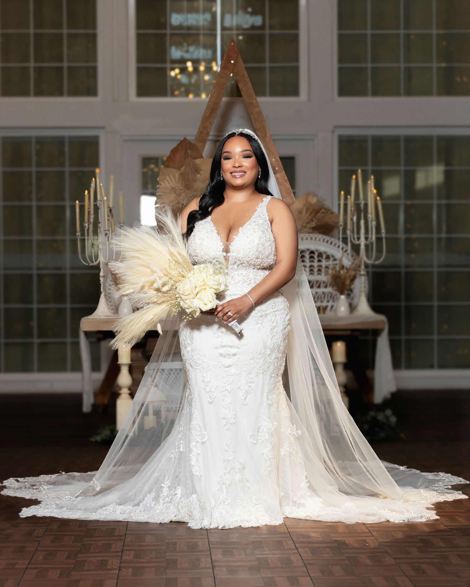 Bride poses in fitted lace wedding gown with dramatic train and dried pampas grass decor.