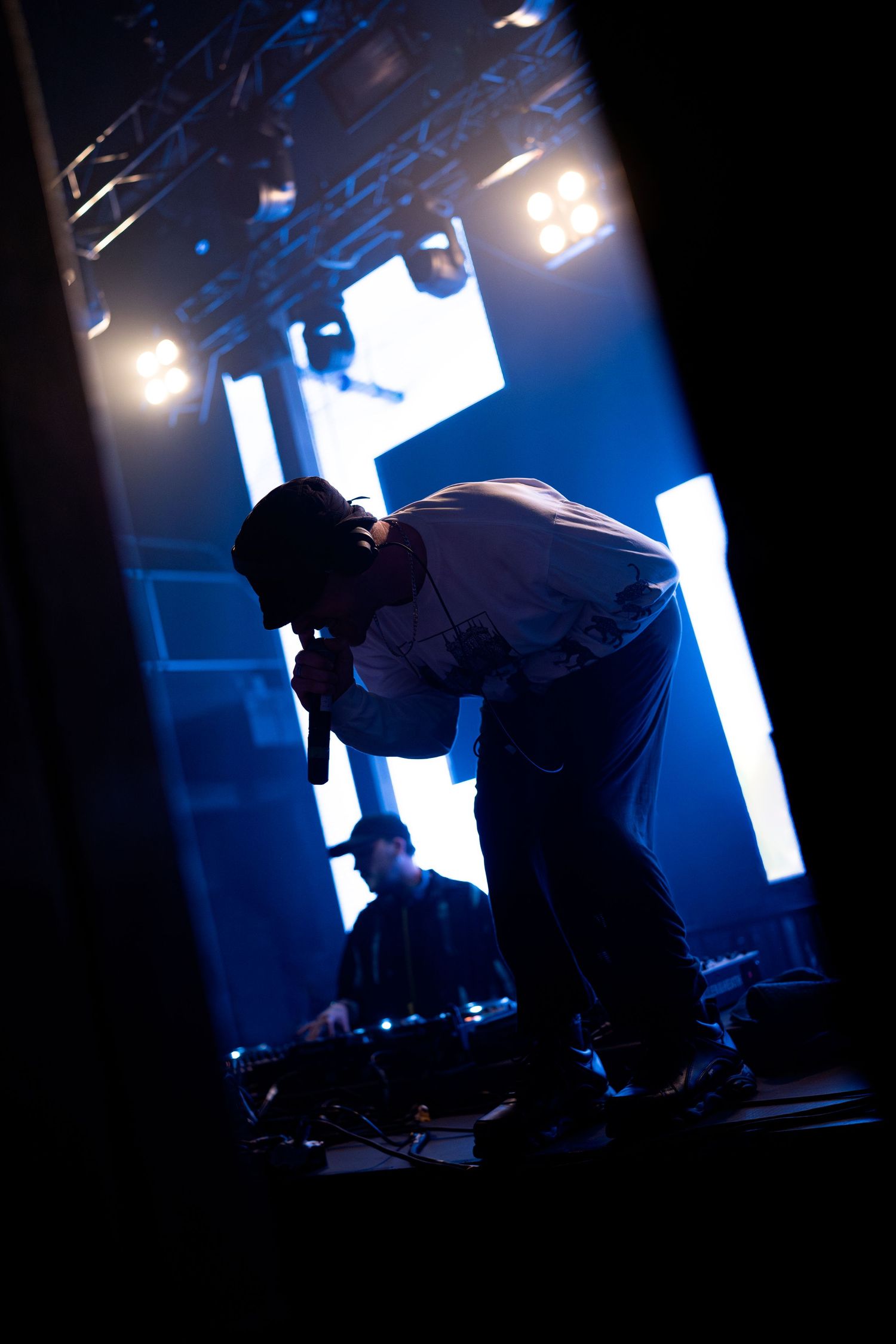 Silhouetted figures perform on a dark stage with striking blue backlighting creating an atmospheric scene.