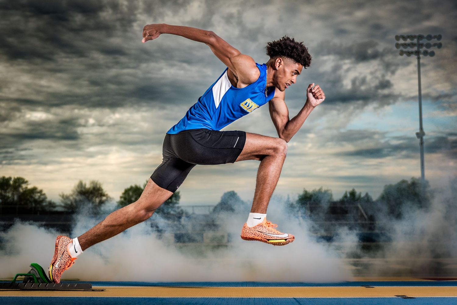 High school track runner preparing on starting block under dramatic sky – athlete portrait Ohio