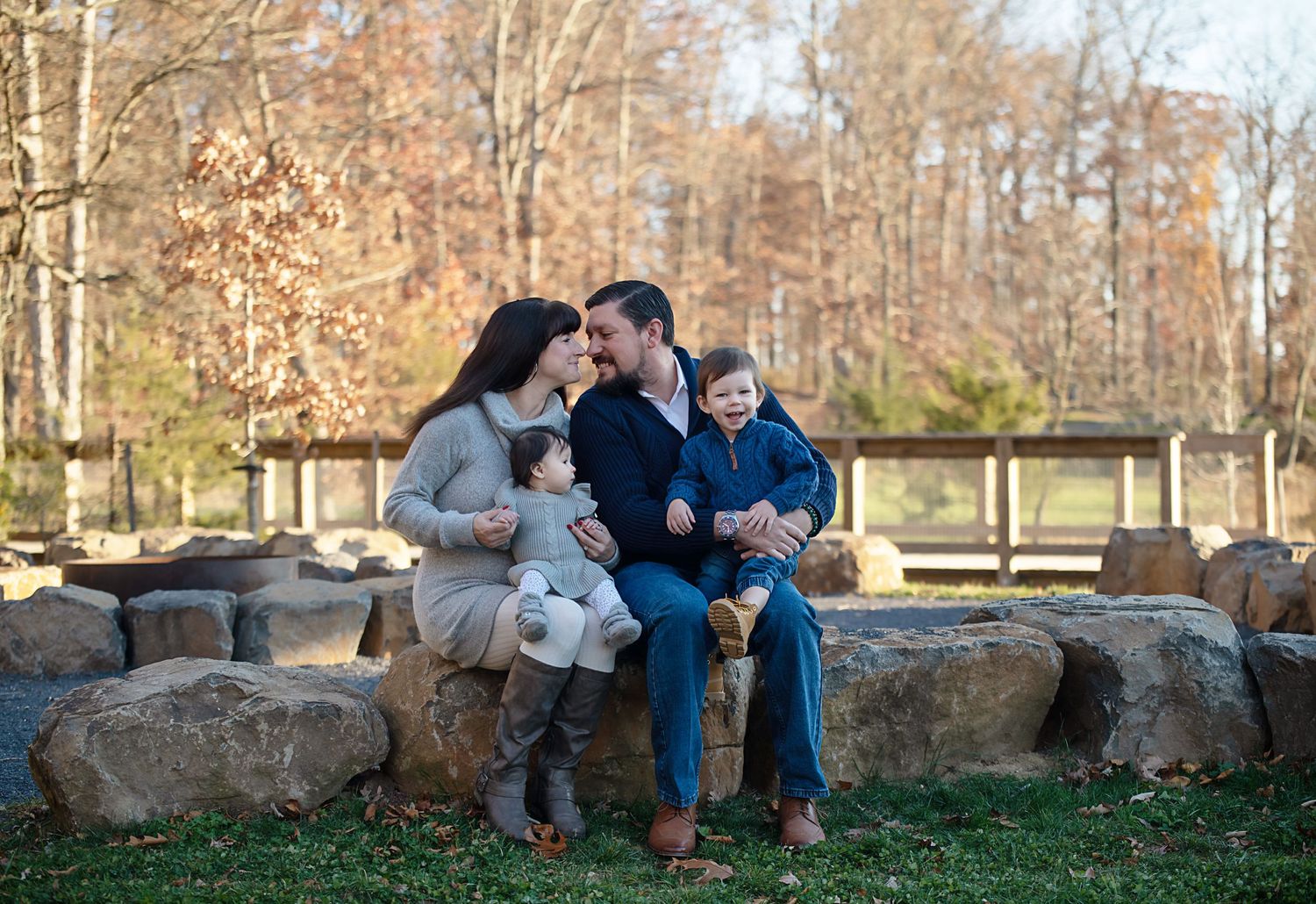 Family sitting together on large rocks in autumn park setting.