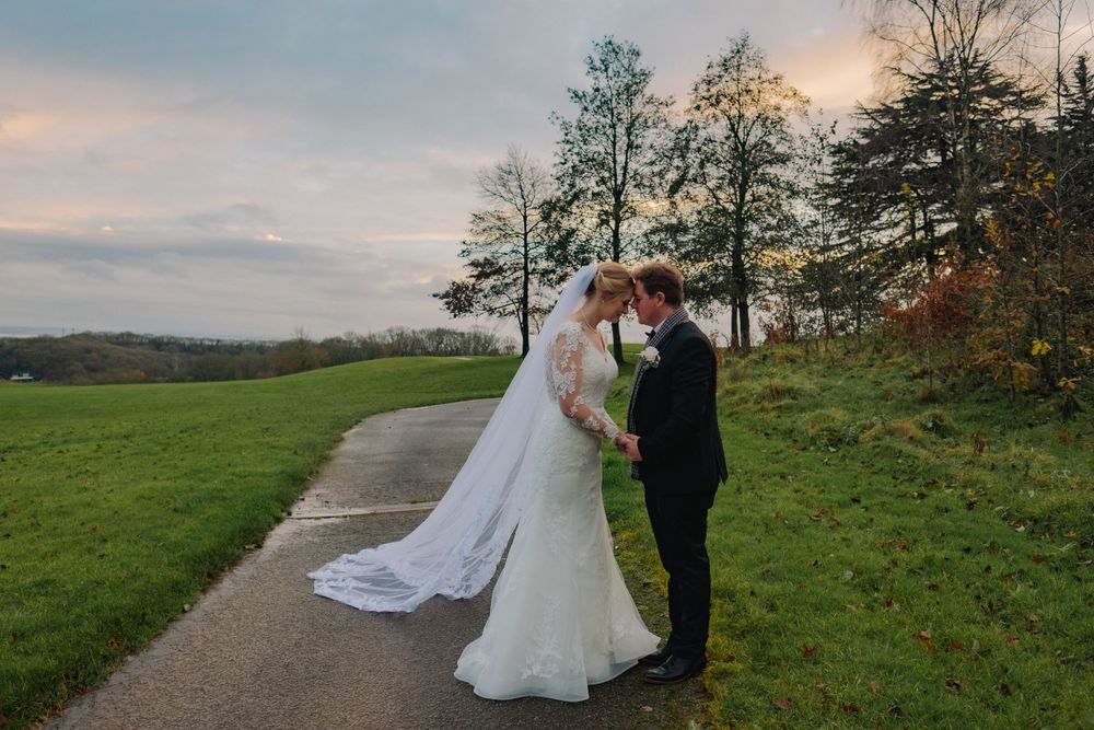 Elegant bride and groom embrace on a scenic hilltop path during their autumn wedding photoshoot.
