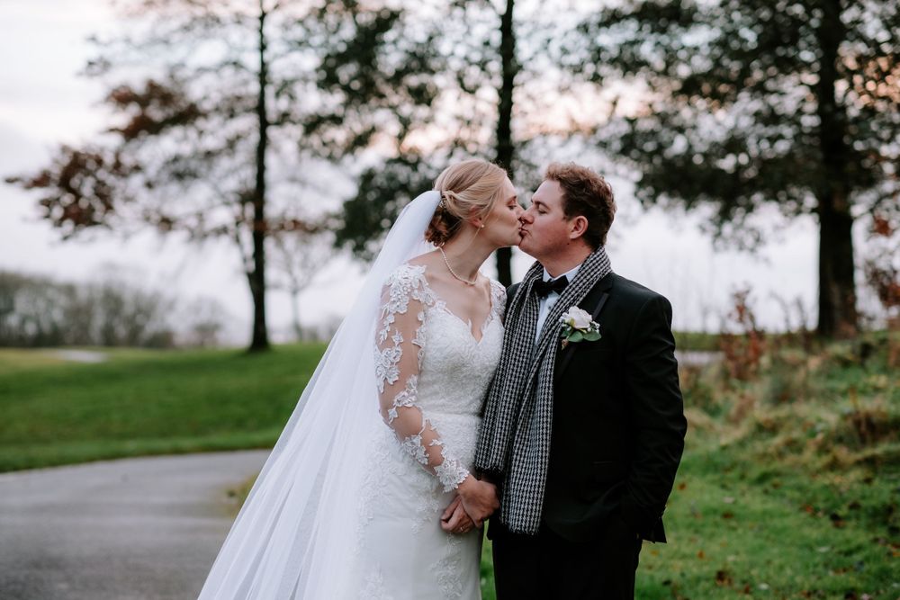 Wedding couple shares romantic moments on a countryside path surrounded by fall foliage.