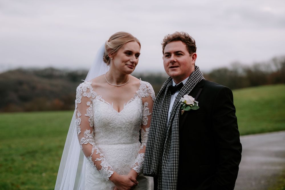 Intimate wedding portraits captured on a rustic path with overcast skies and rolling hills.